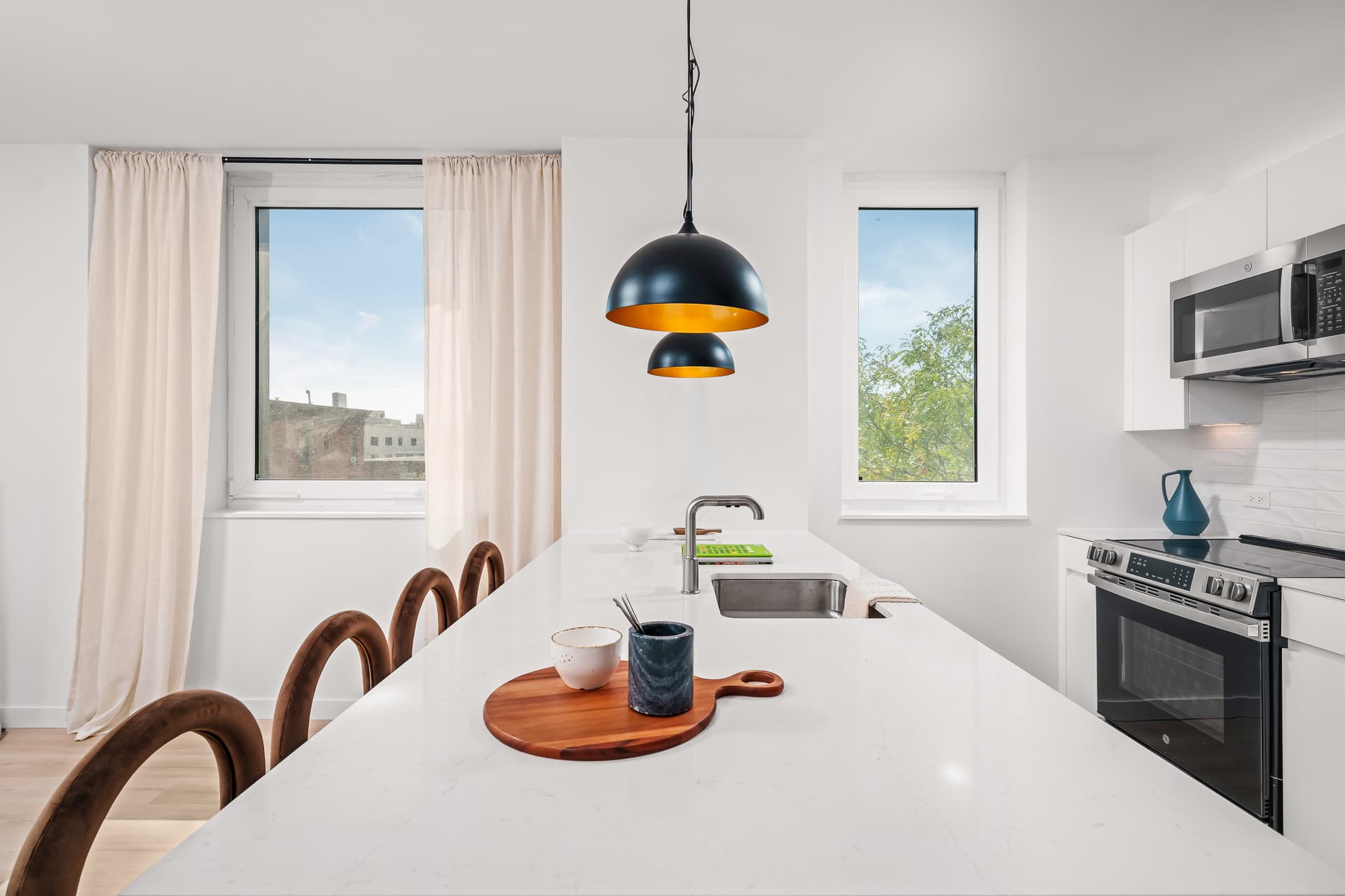 Kitchen at Prisma House: a white quartz island with velvet stools under two black pendant lamps, windows on both sides